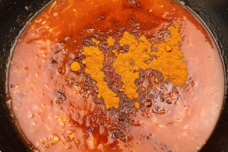 Zu den gebratenen Gemüsestreifen kommt Tomatenpüree, Wasser und Gewürze in die Pfanne. 